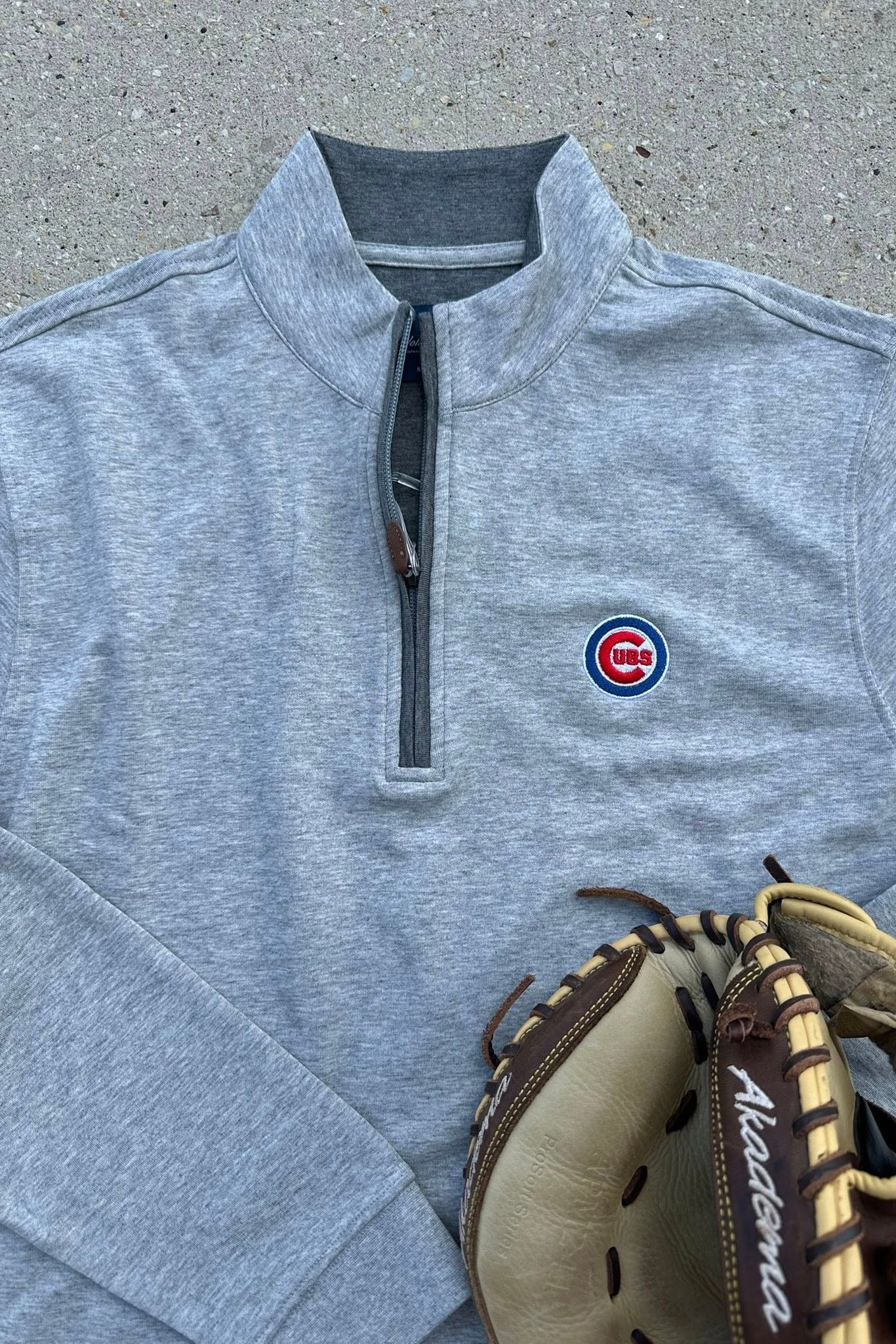 Gray pullover with a logo and a baseball glove on a concrete surface
