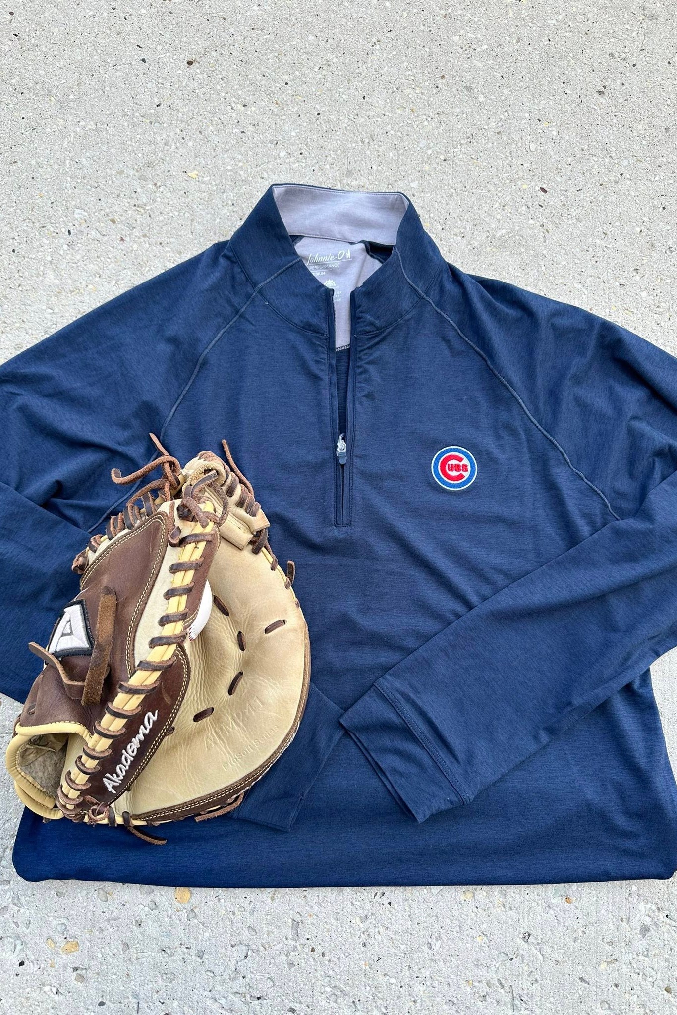 Blue pullover with a logo and a baseball glove on a gray surface