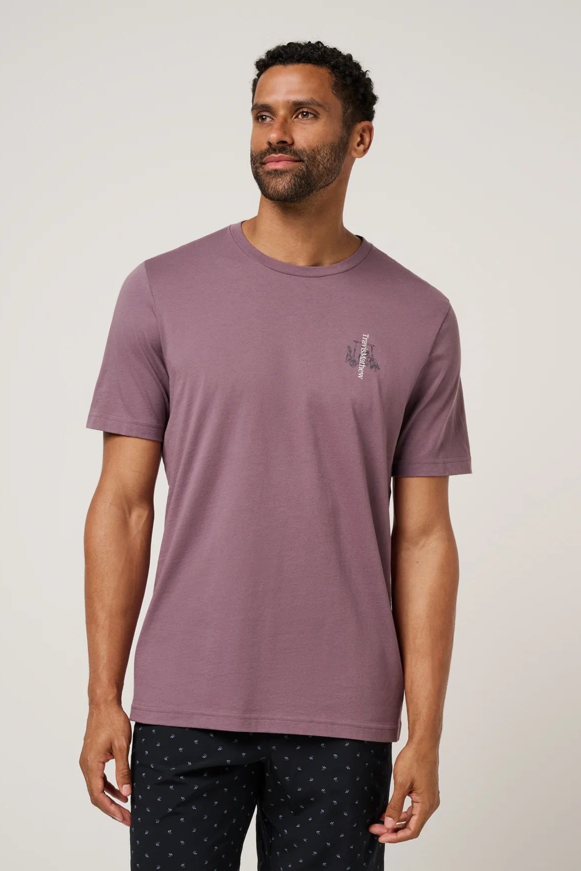 Man wearing a mauve t-shirt with a small logo on a plain background