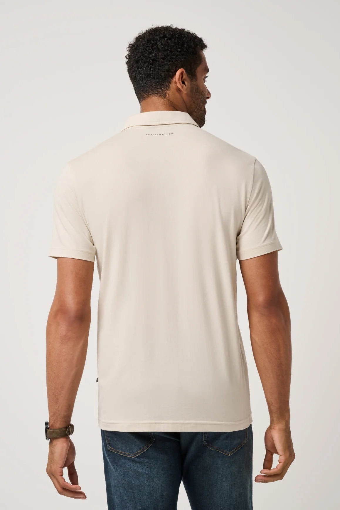 Man wearing a beige polo shirt and dark jeans on a light gray background