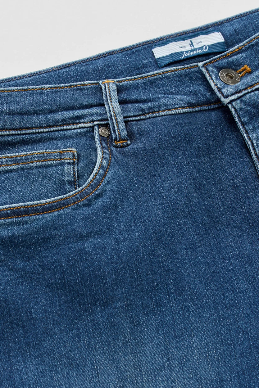 Close-up of blue denim jeans showing the waistband, belt loops, front pocket, and stitching details.