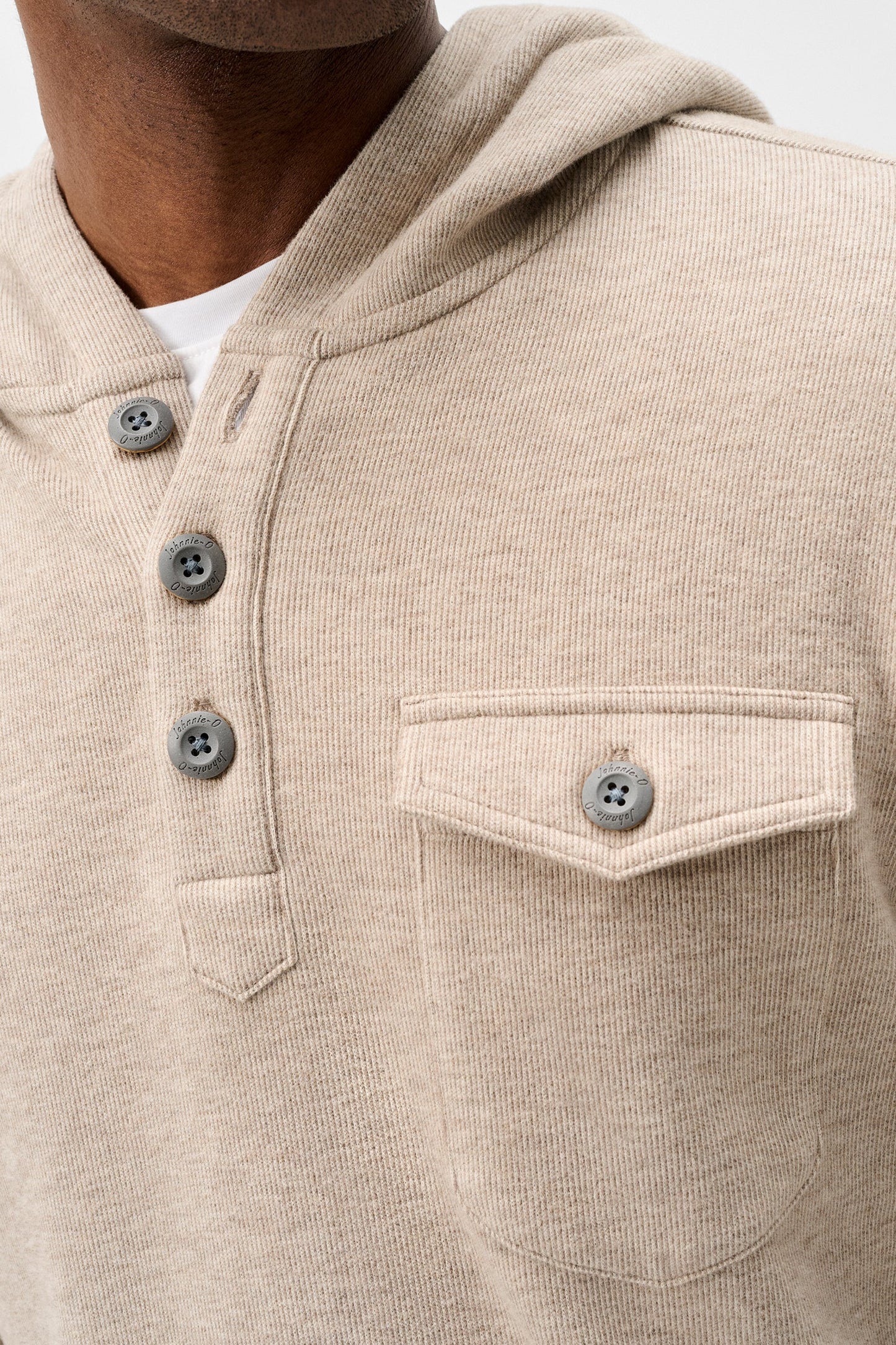 Close-up of a beige ribbed knit hooded pullover sweater with a three-button henley neckline and a chest pocket, worn by a model.