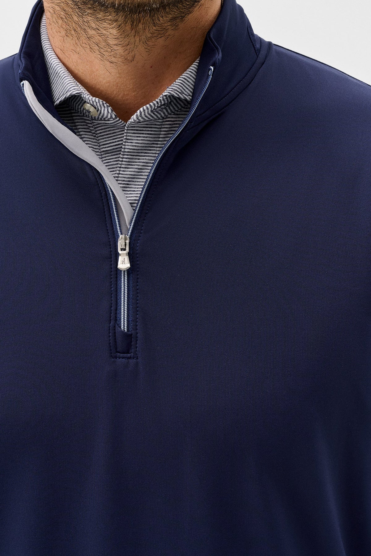 Close-up of a man wearing a navy blue quarter-zip pullover over a striped collared shirt, shown against a light gray studio background.