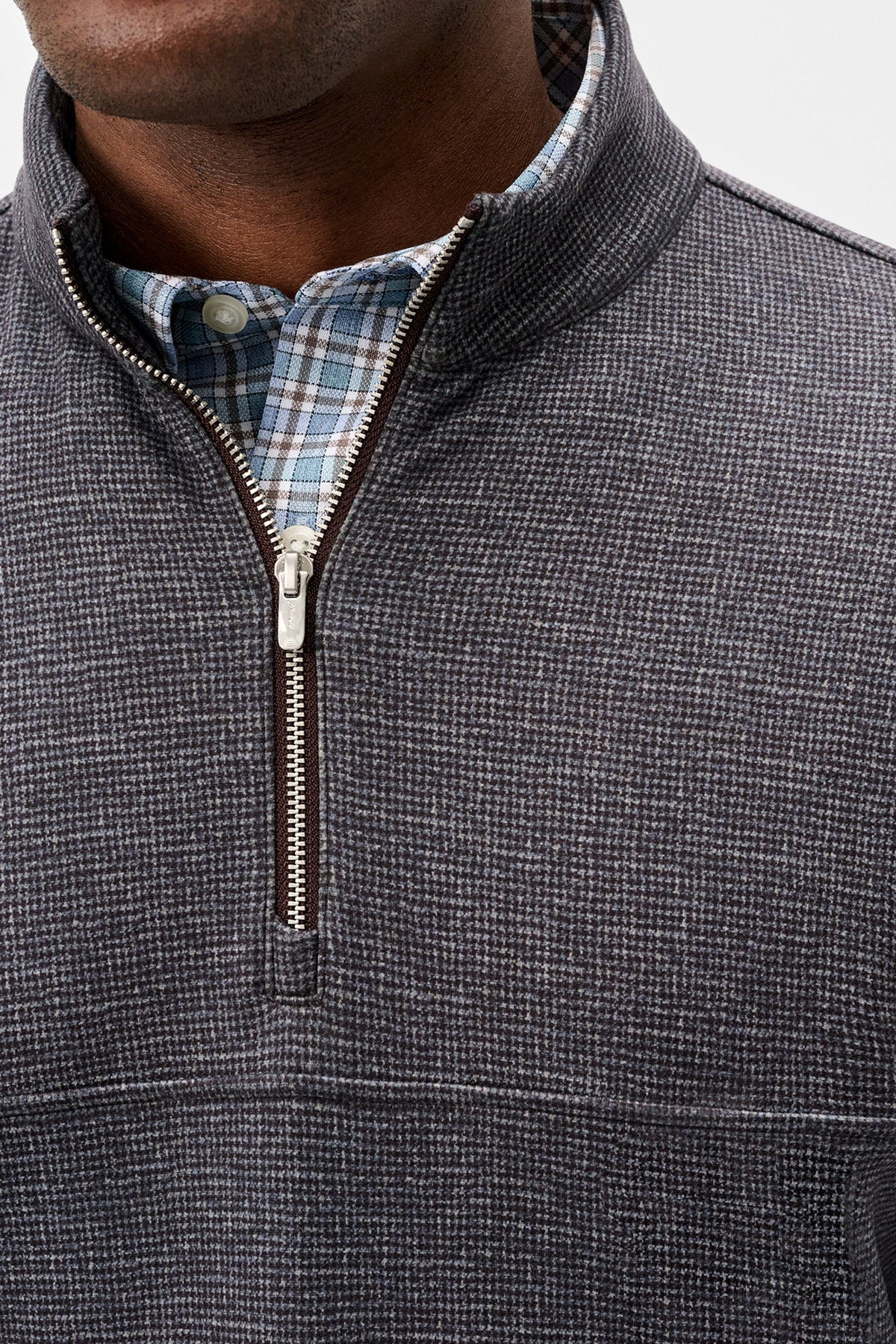 Close-up of a man wearing a charcoal gray textured quarter-zip pullover sweater over a blue and white plaid button-down shirt.