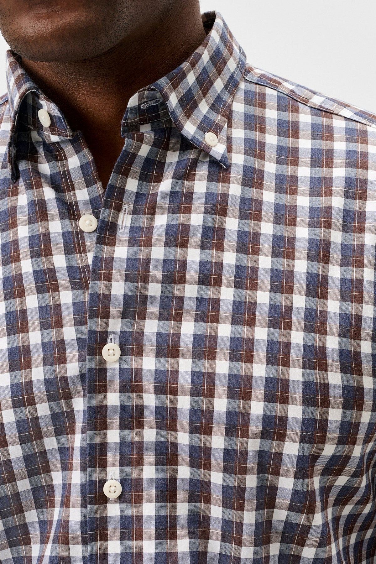 Close-up of a man wearing a plaid button-down shirt with a blue, brown, and white checkered pattern.