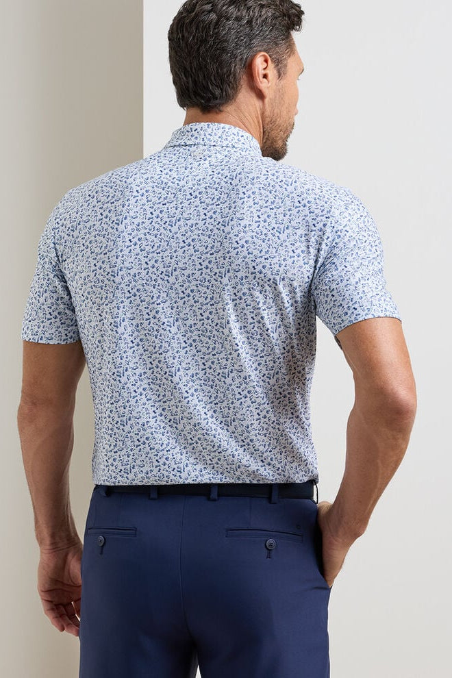 Man wearing a blue patterned shirt and navy pants against a plain background