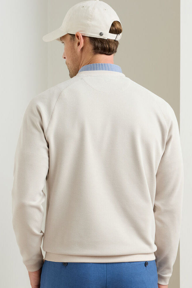 Man wearing a beige sweater and white cap, facing away from the camera on a plain background