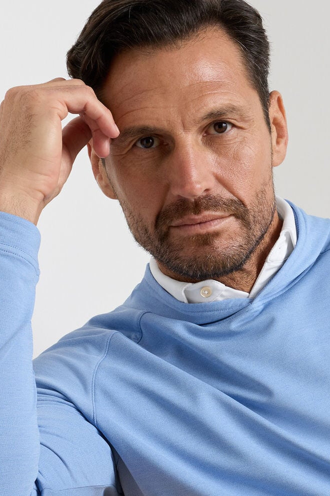 Man wearing a light blue sweater over a white shirt against a plain background