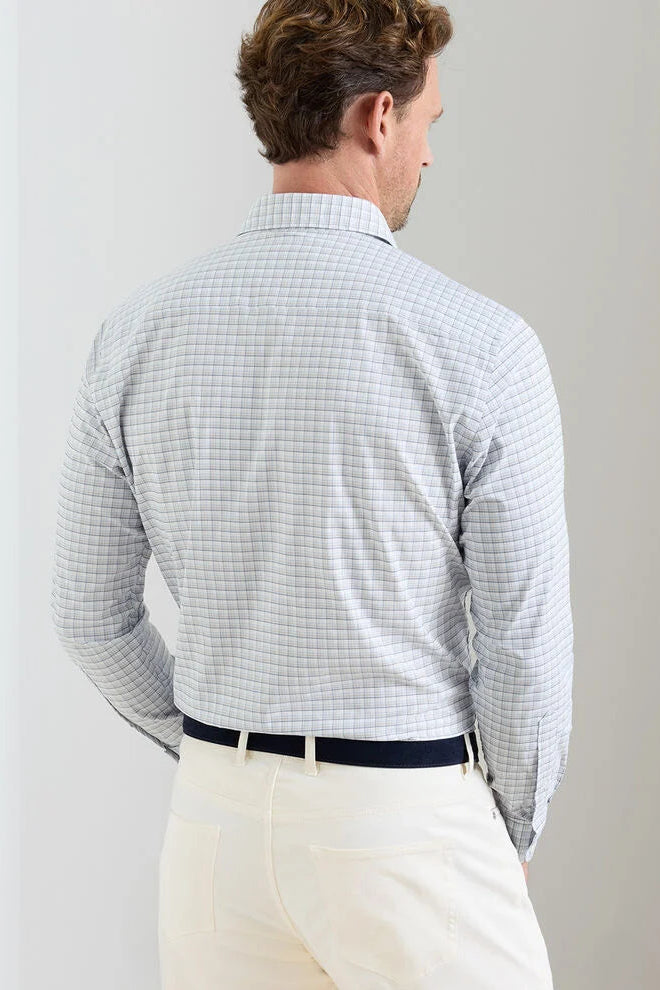 Man wearing a light blue checkered shirt and white pants against a plain background
