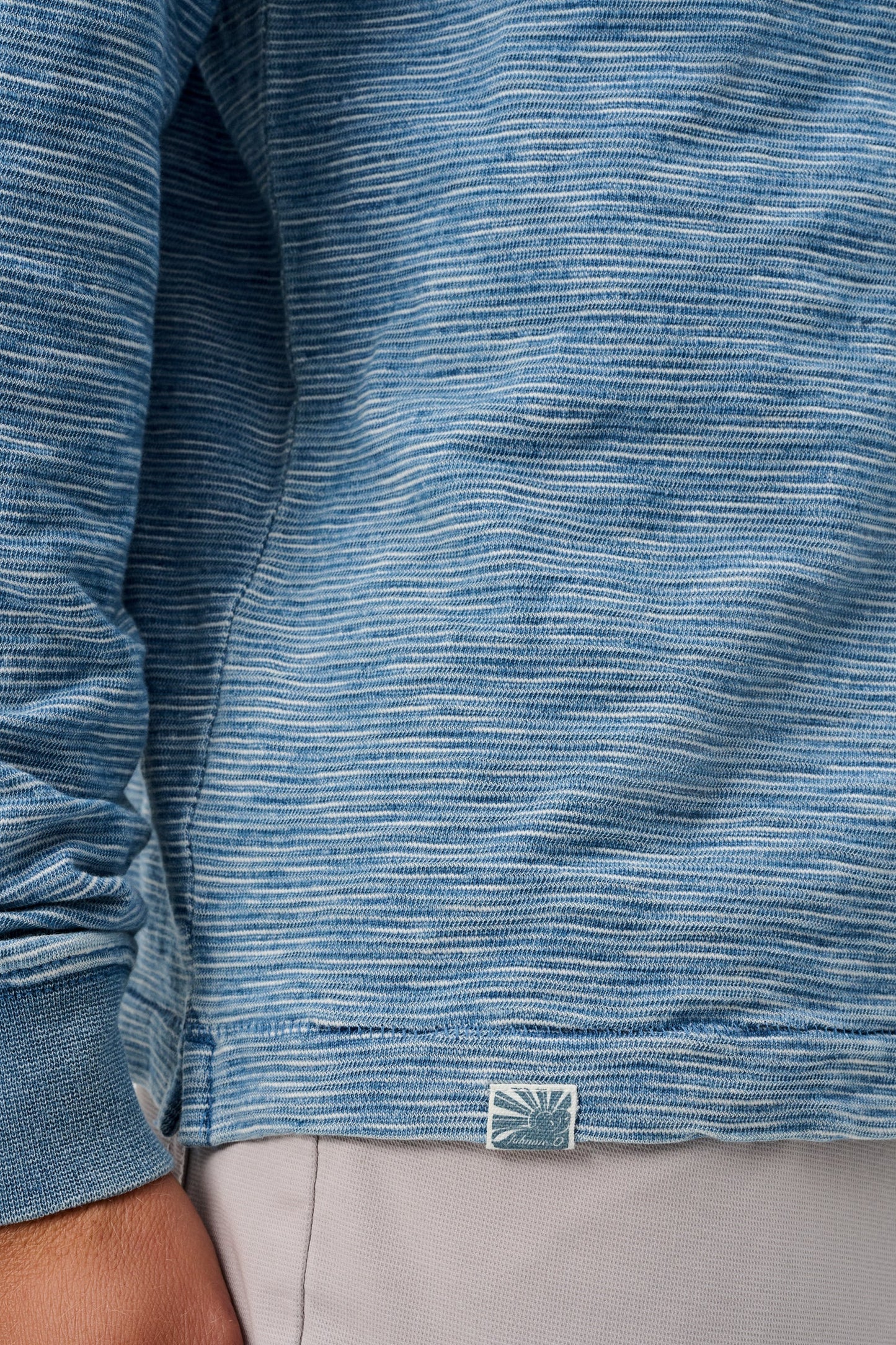 Close-up of a blue textured shirt with a brand logo on a person wearing gray pants.