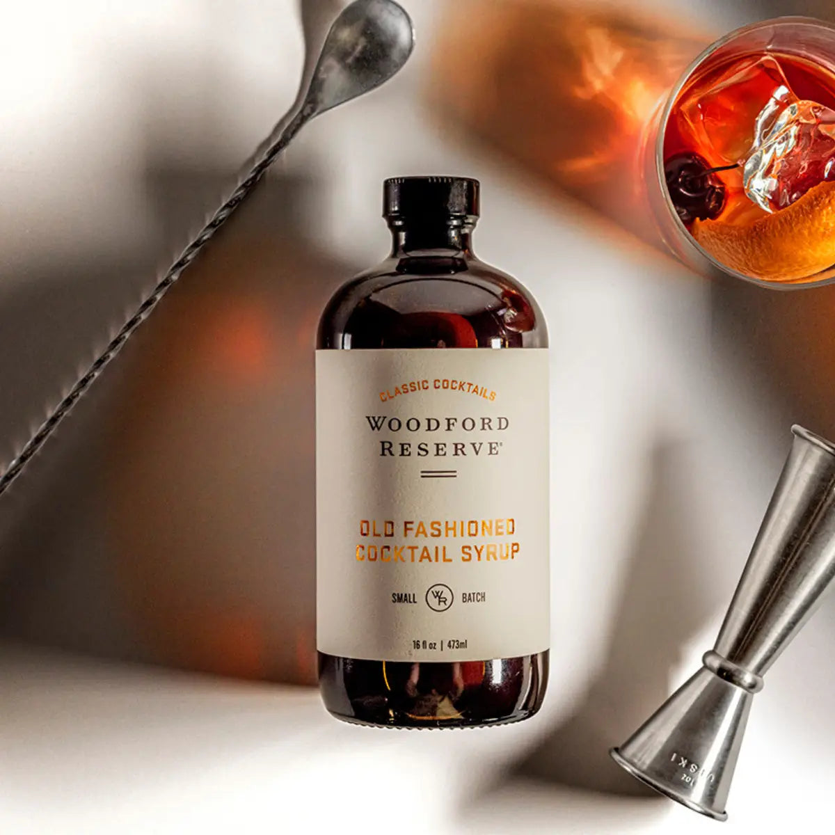 Woodford Reserve Old Fashioned Cocktail Syrup bottle with a cocktail and bar tools in the background