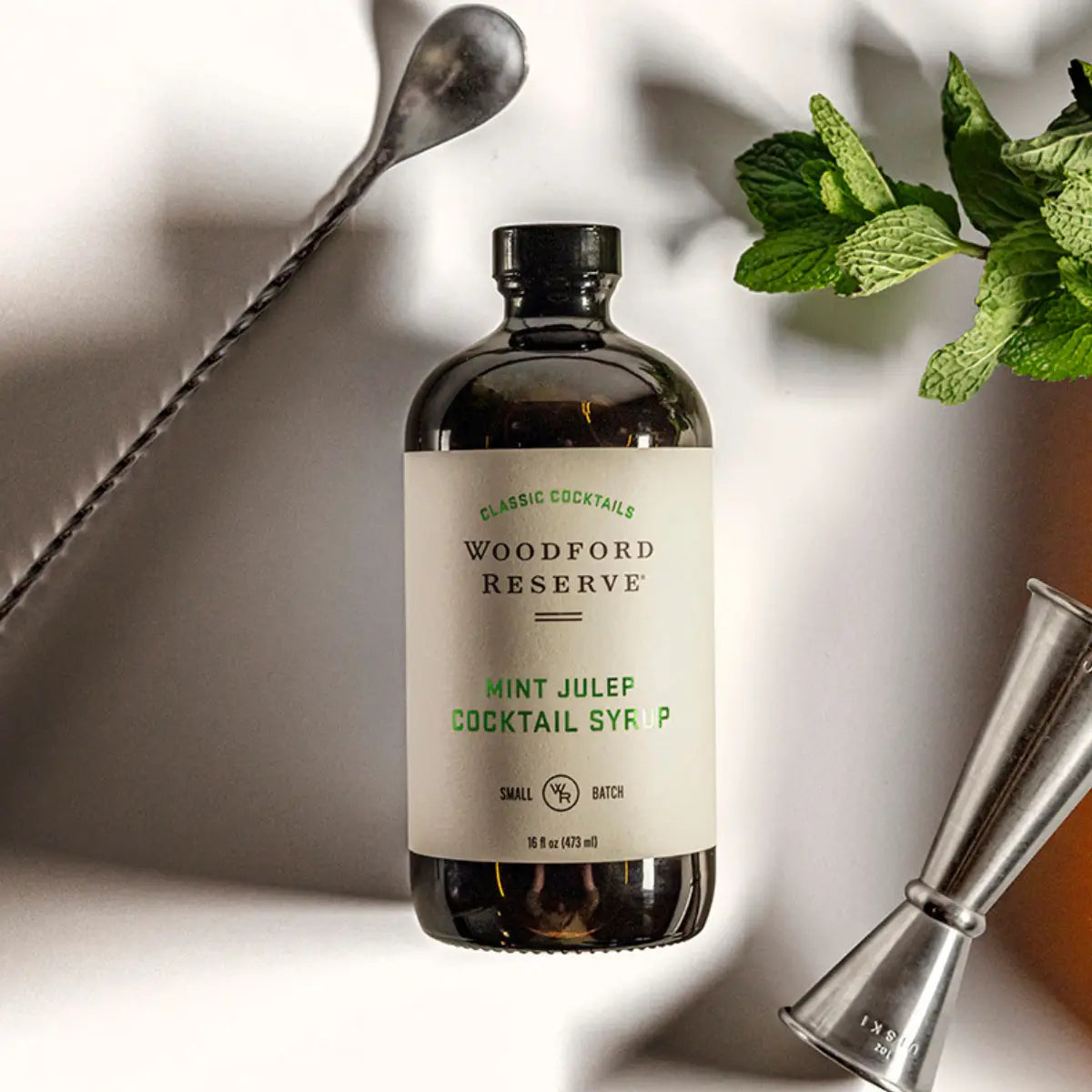 Woodford Reserve Mint Julep Cocktail Syrup bottle with mint leaves and a jigger on a light background