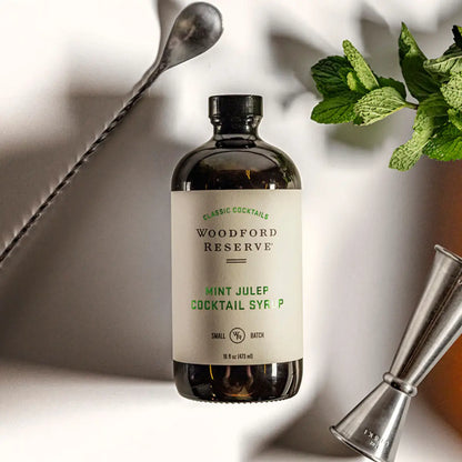 Woodford Reserve Mint Julep Cocktail Syrup bottle with mint leaves and a jigger on a light background