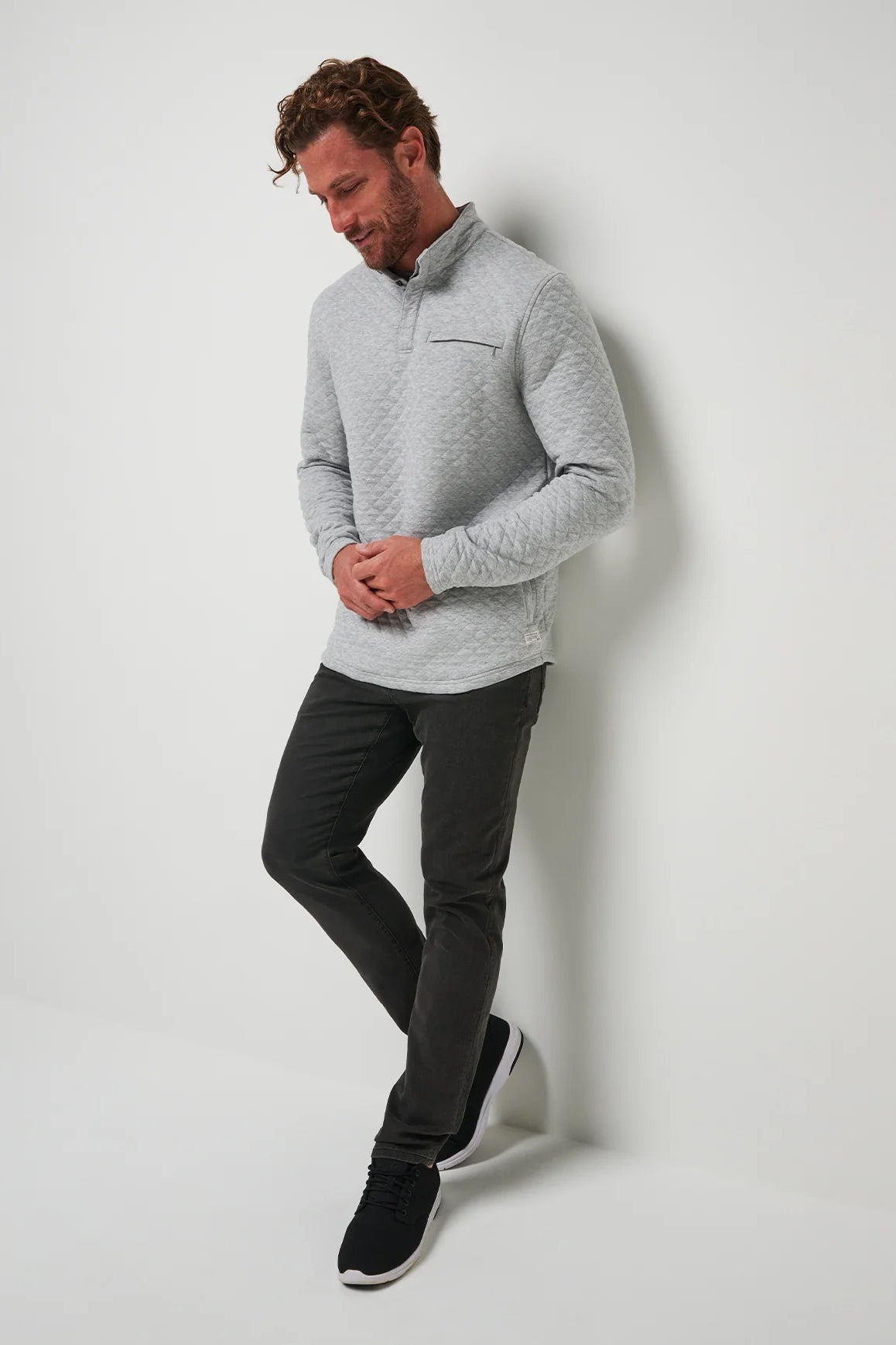 Man wearing a gray sweater and black pants against a white background