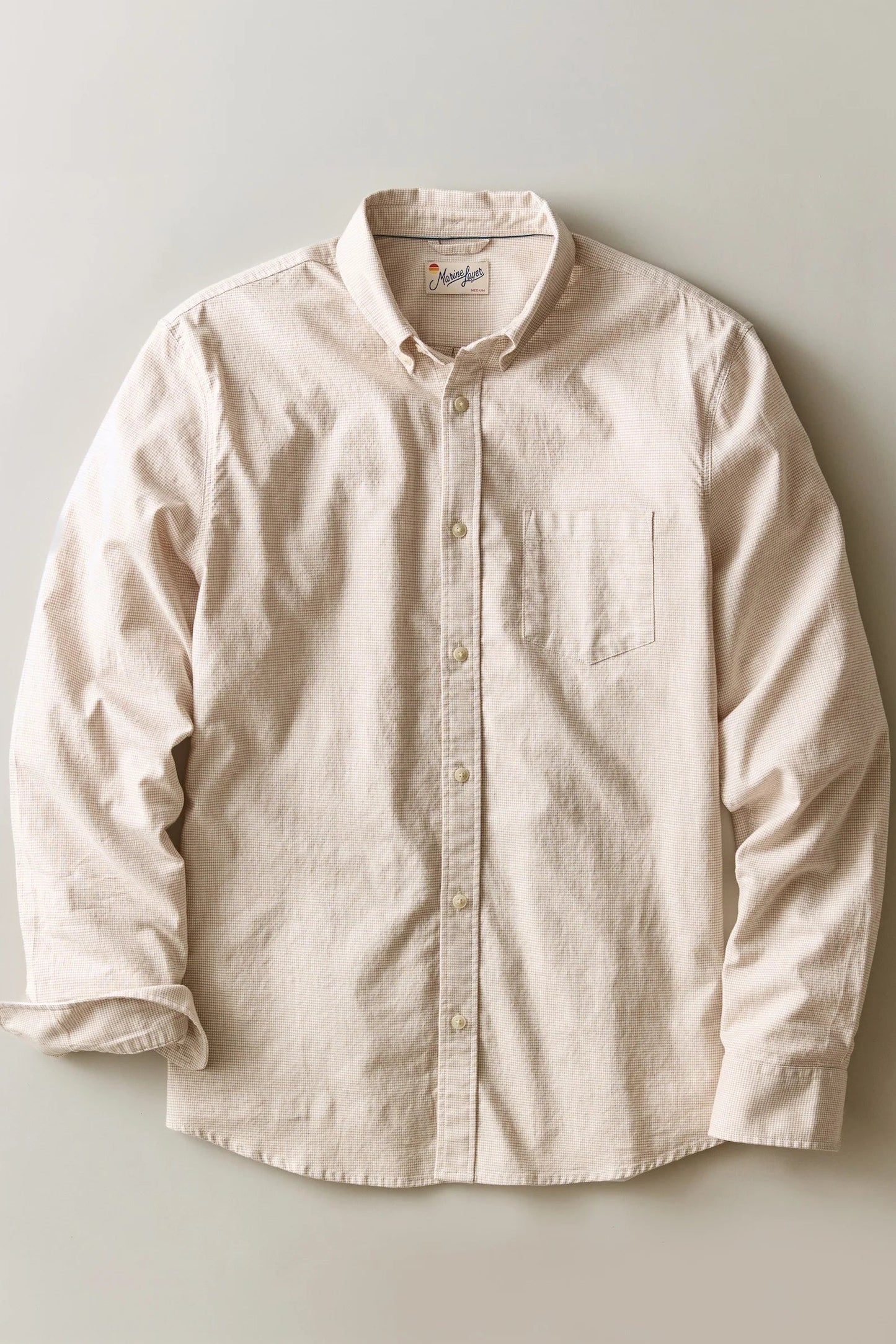 A light beige long-sleeve button-down shirt with a single chest pocket, laid flat against a neutral light gray background.