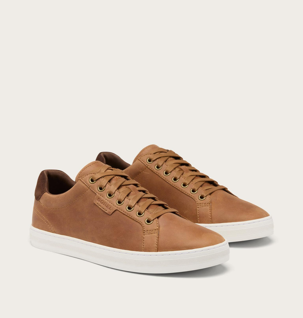 A pair of low-top casual sneakers in tan leather with matching laces and white rubber soles, photographed on a clean off-white studio background.