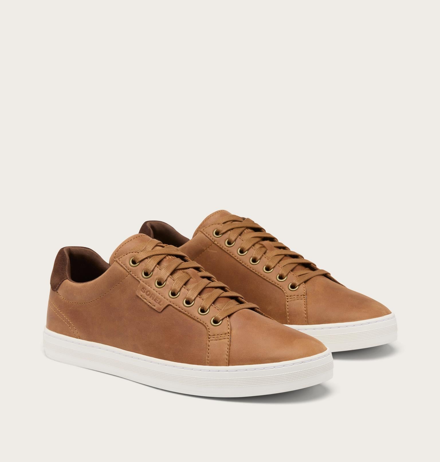 A pair of low-top casual sneakers in tan leather with matching laces and white rubber soles, photographed on a clean off-white studio background.