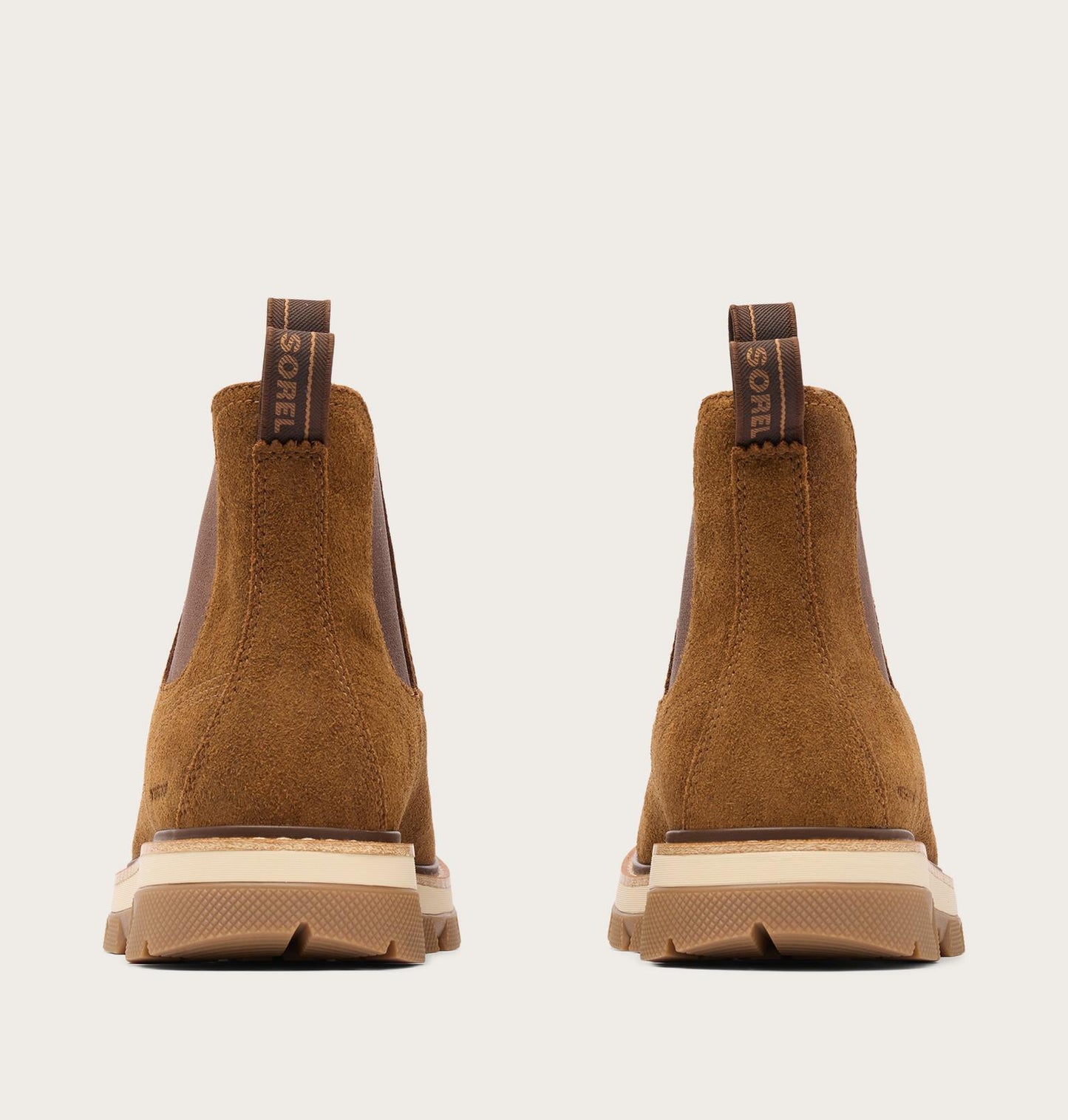 A pair of brown suede Chelsea-style boots shown from the back, featuring elastic side panels, pull tabs with the SOREL brand name, and chunky beige and brown soles, set against a light gray background.