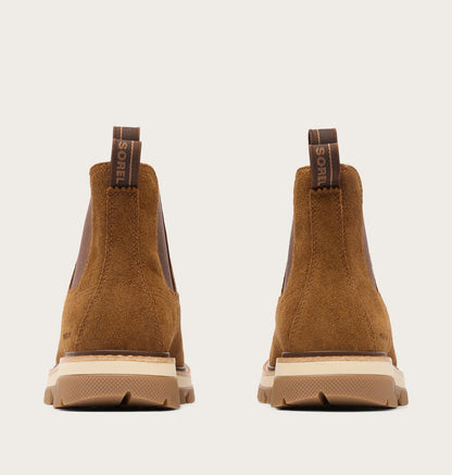 A pair of brown suede Chelsea-style boots shown from the back, featuring elastic side panels, pull tabs with the SOREL brand name, and chunky beige and brown soles, set against a light gray background.