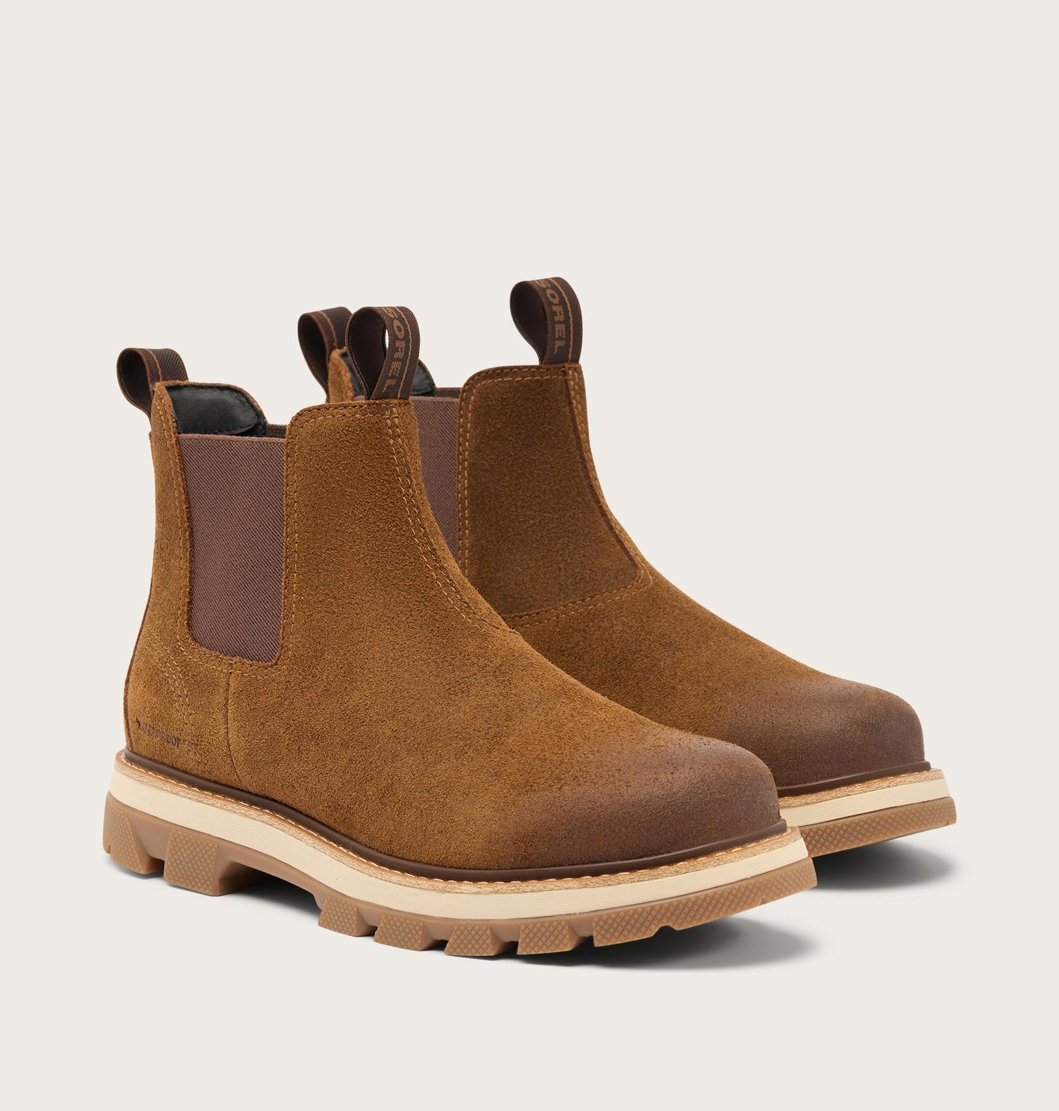 A pair of brown suede Chelsea boots with elastic side panels and pull tabs, featuring a chunky beige lug sole, shown on a light beige background.