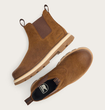 A pair of brown suede Chelsea-style boots shown from top and side views on a light gray background. One boot shows a dark brown elastic side panel, a tan midsole, and pull tabs.