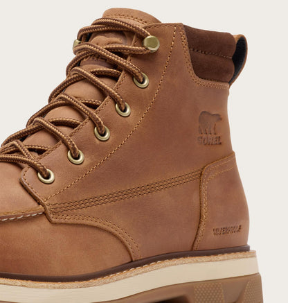 A close-up of a brown suede high-top work boot by All In Style, featuring matching brown laces, brass eyelets, a debossed bear logo on the side, and a thick beige and brown sole.