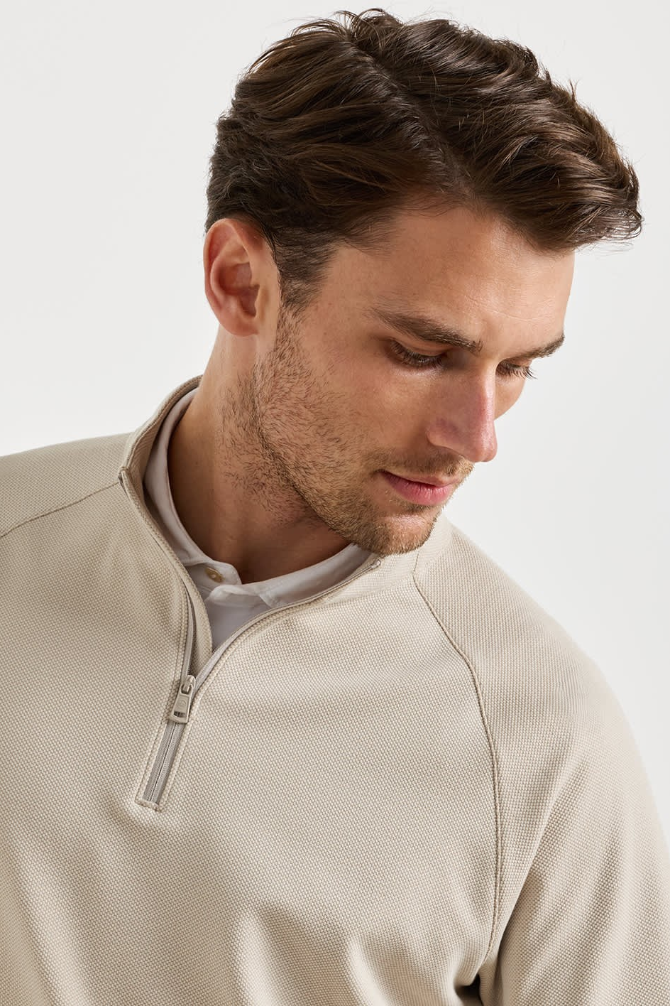 A man wearing a light beige quarter-zip pullover sweater over a white collared shirt, photographed against a clean white studio background.