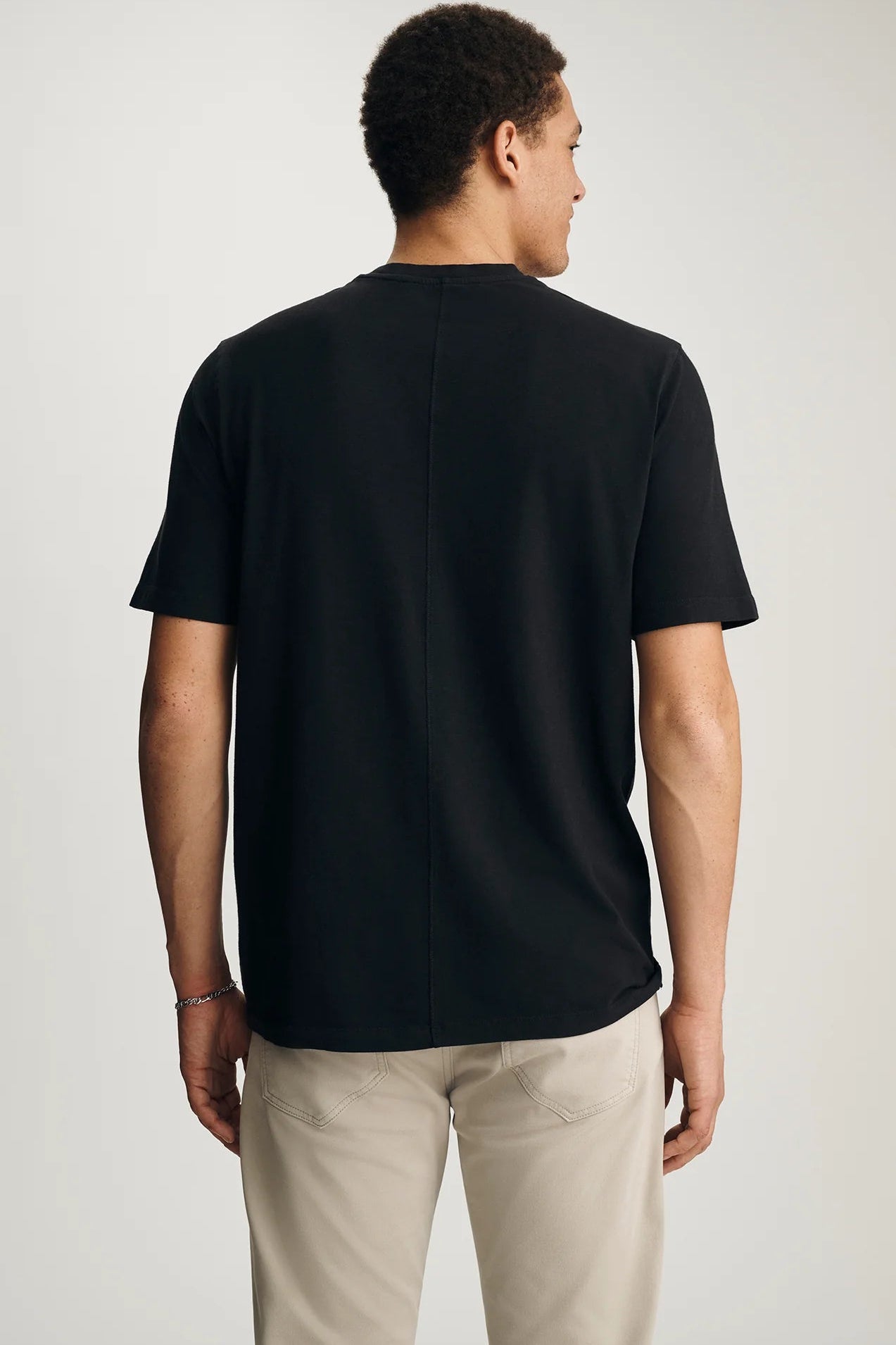 Person wearing a black t-shirt and beige pants on a light gray background