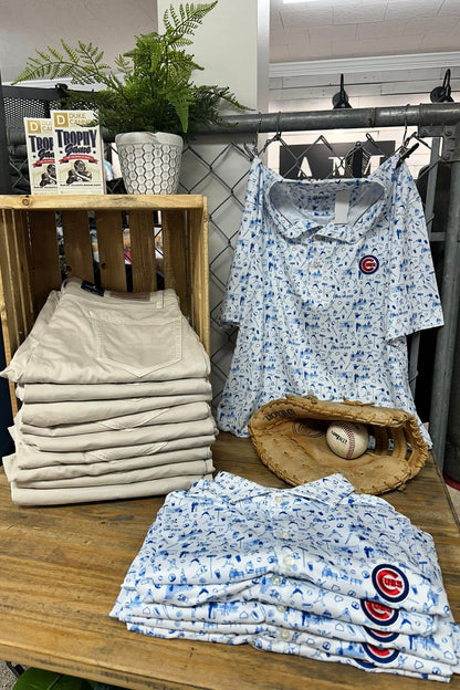 Stacked folded shirts with a baseball glove and ball on a wooden table.