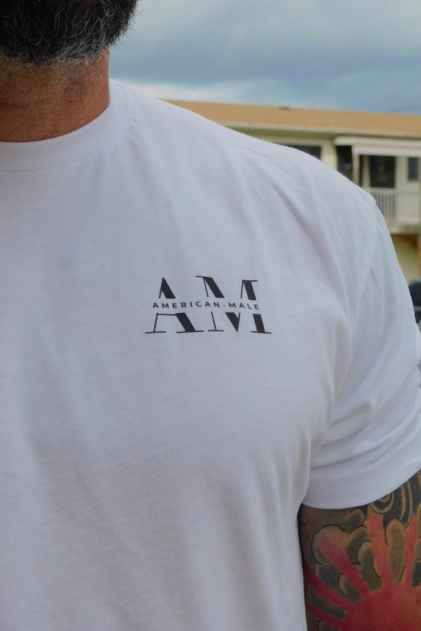 Person wearing a white t-shirt with 'AMERICAN MALE' text, standing outdoors.