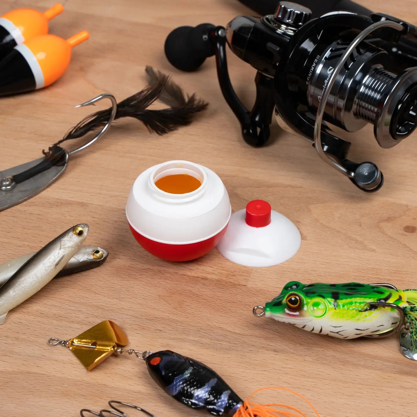 Fishing gear including a reel, lures, and a bobber on a wooden surface.