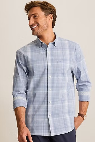 A man wearing a light blue and white plaid long-sleeve button-down shirt, shown from the waist up against a plain light beige studio background.