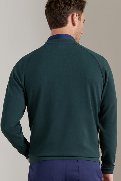 A man viewed from behind wearing a dark green long-sleeve quarter-zip pullover with a contrasting navy blue collar, paired with navy trousers, against a plain beige studio background.