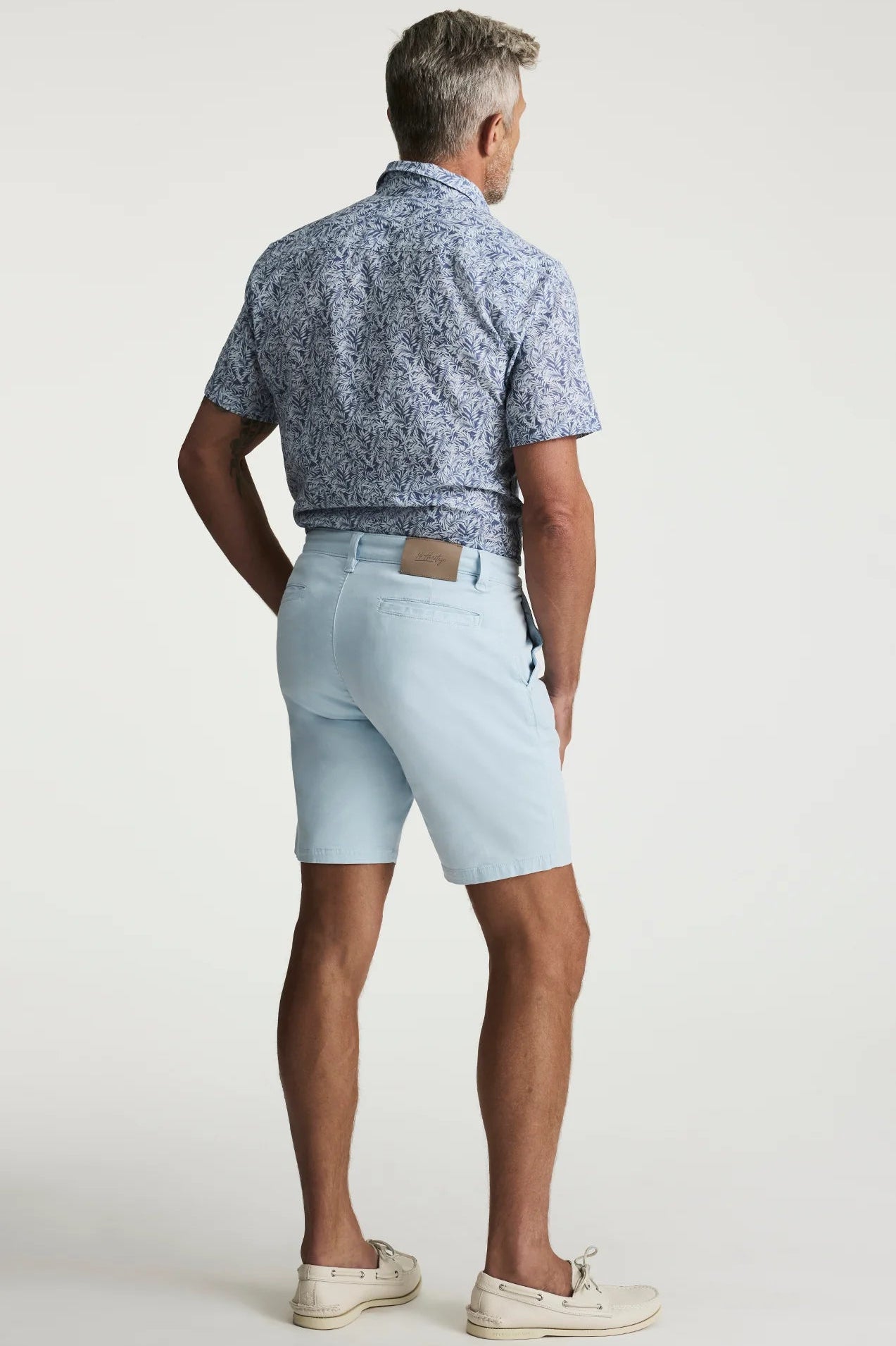 Man wearing a patterned blue shirt and light blue shorts on a white background