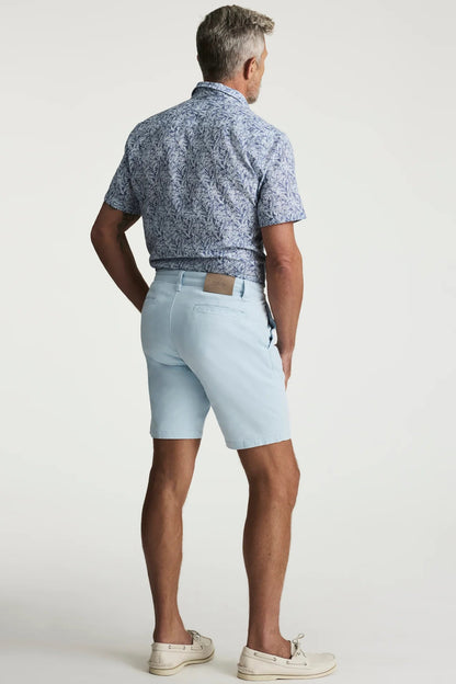 Man wearing a patterned blue shirt and light blue shorts on a white background