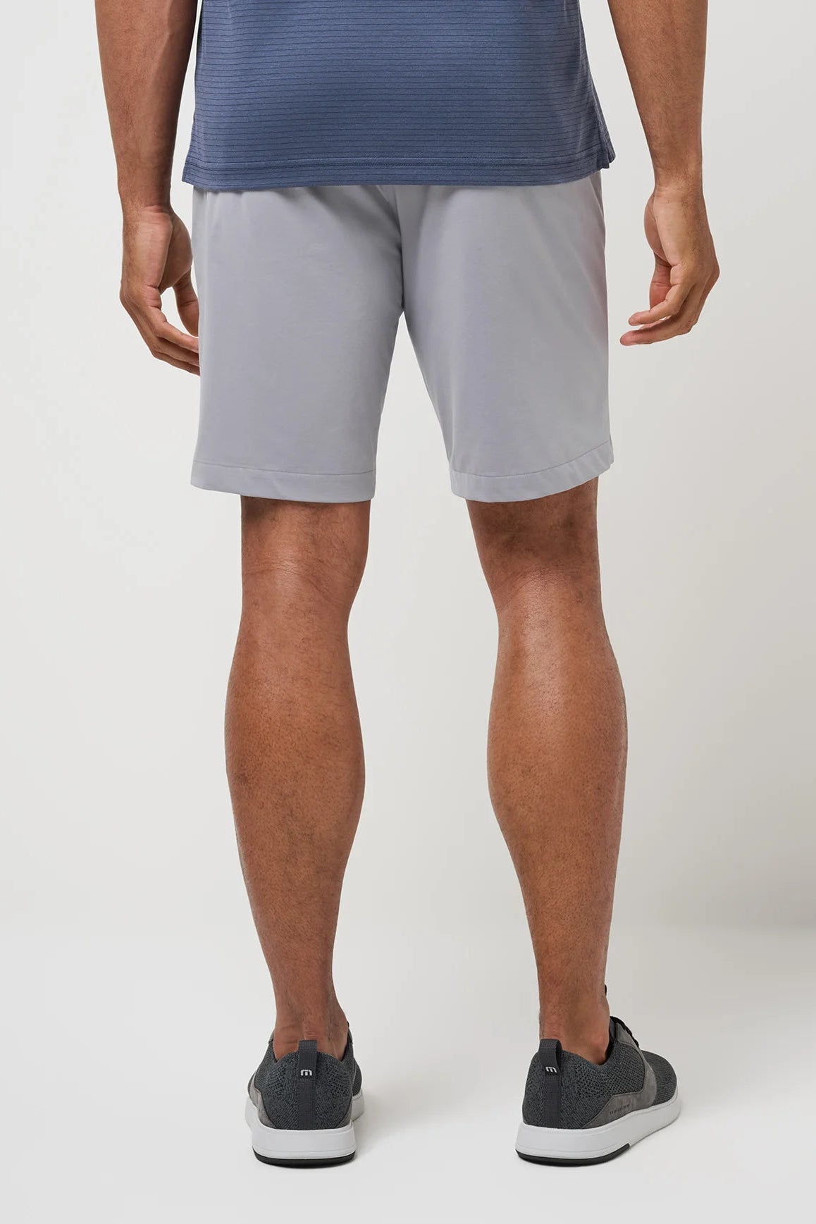 Person wearing gray shorts and dark shoes on a white background