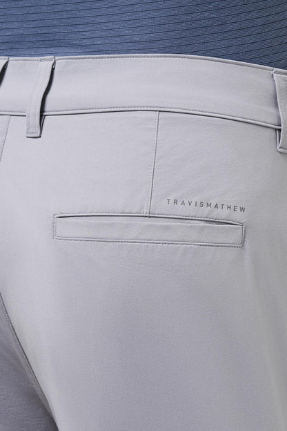 Light gray pants with 'Travis Mathew' branding on a blue shirt background