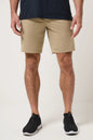 A man wearing beige athletic shorts, a navy blue t-shirt, and black sneakers, shown from the waist down against a light off-white studio background.