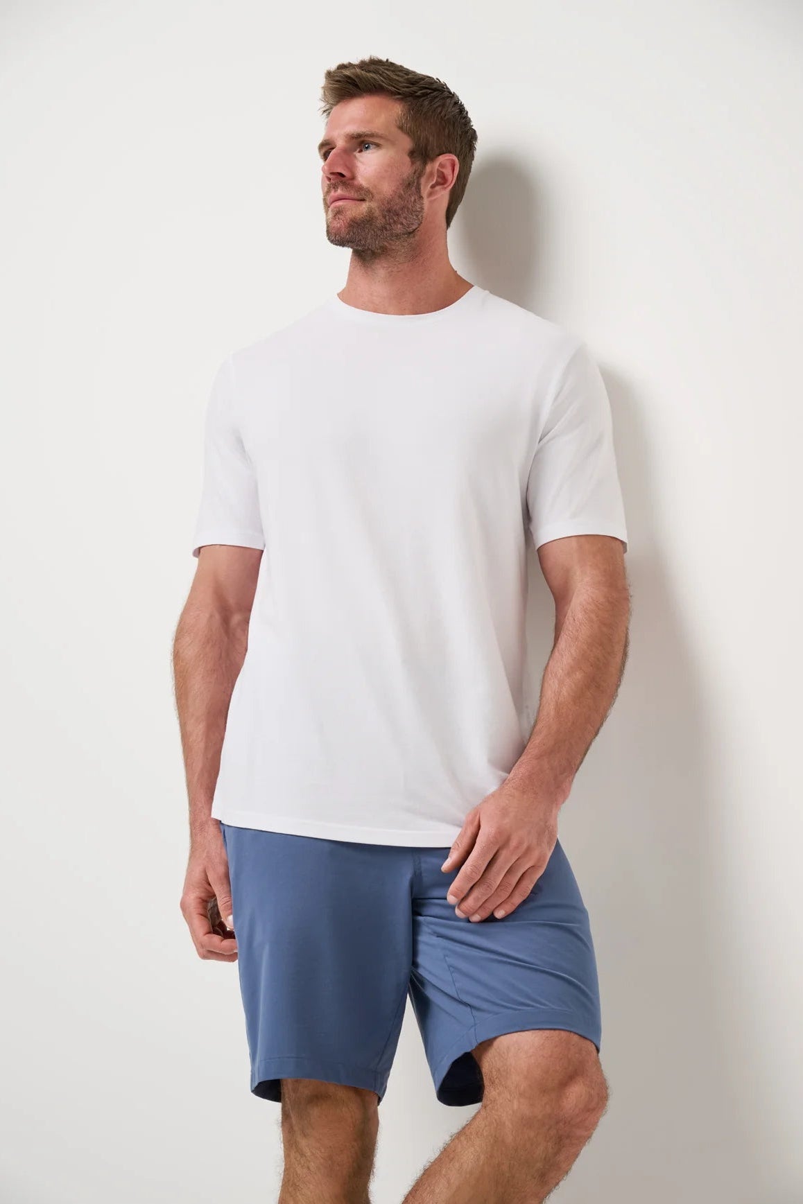 Man wearing a white t-shirt and blue shorts against a plain background