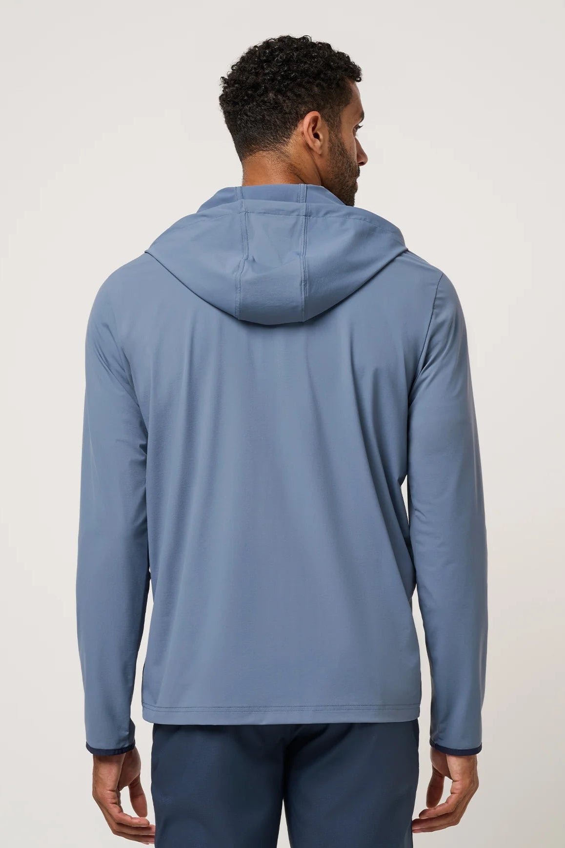 Man wearing a blue hoodie from behind on a light gray background