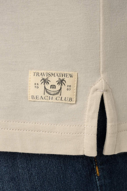 Close-up of a label on a garment with 'Travismathew Beach Club' text and palm tree design.