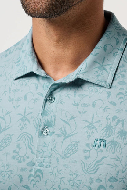 Close-up of a light blue patterned polo shirt with a brand logo on a neutral background