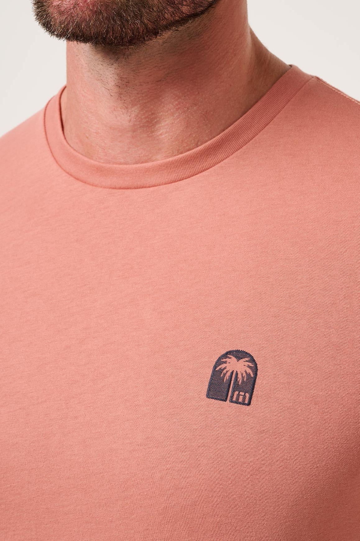 Close-up of a person wearing a pink t-shirt with a small logo on the chest.