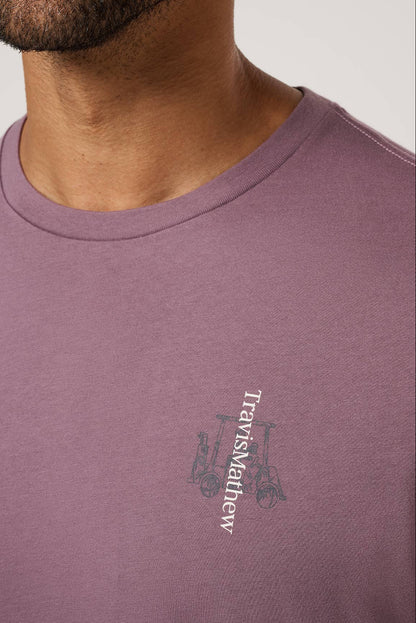 Close-up of a person wearing a purple Travis Mathew t-shirt with a logo.