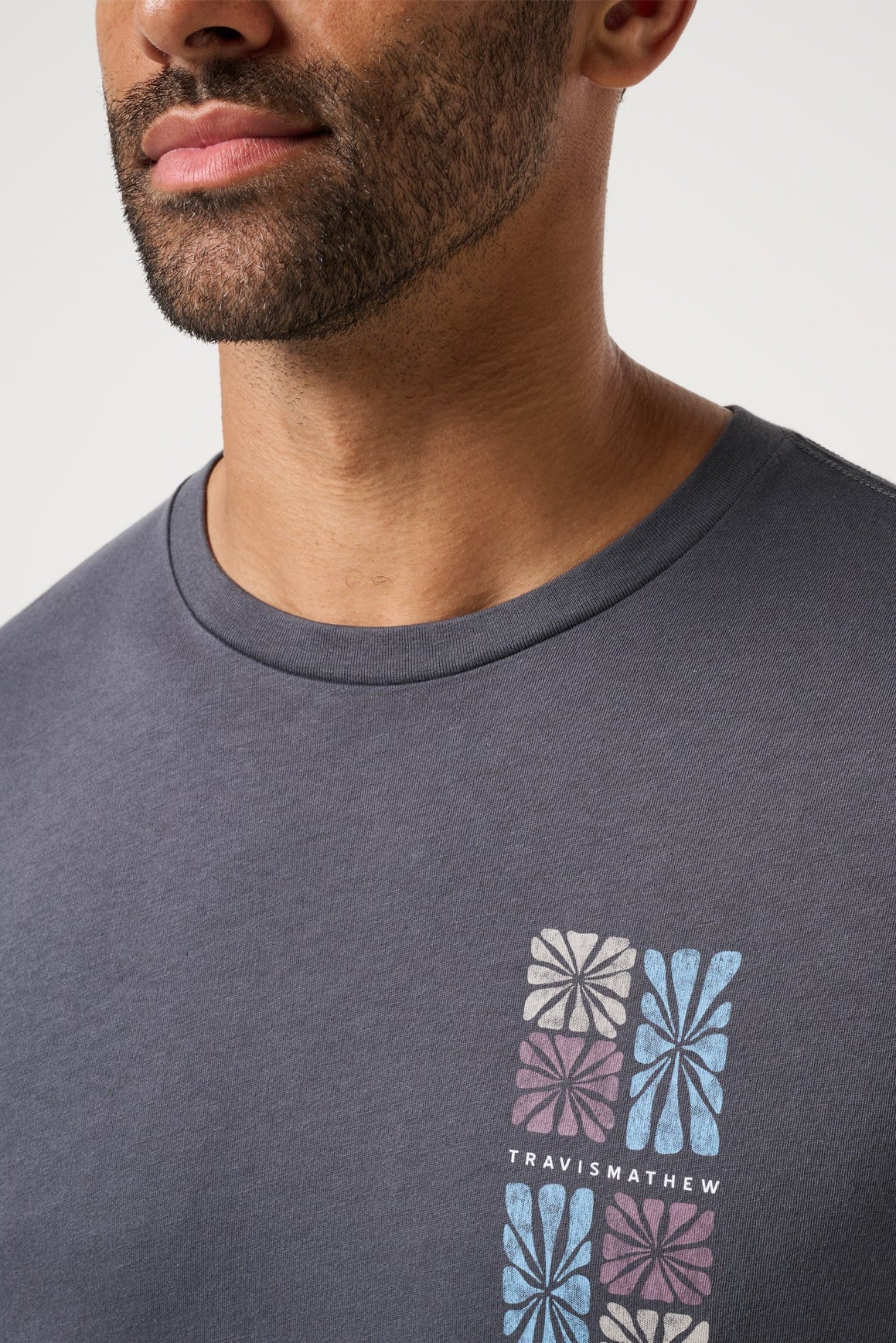 Man wearing a dark gray t-shirt with a colorful geometric pattern and 'Travis Mathew' branding.