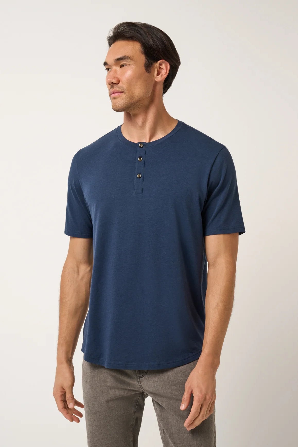 Man wearing a blue henley shirt and gray pants on a white background