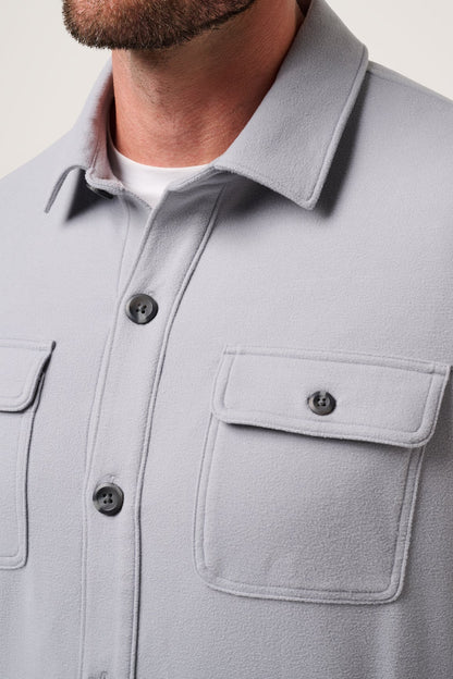 Close-up of a light gray shirt with collar and pockets on a neutral background