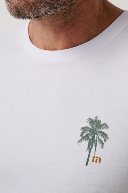 Close-up of a man wearing a white crew-neck t-shirt with a small green palm tree graphic and a gold 'm' logo on the left chest.