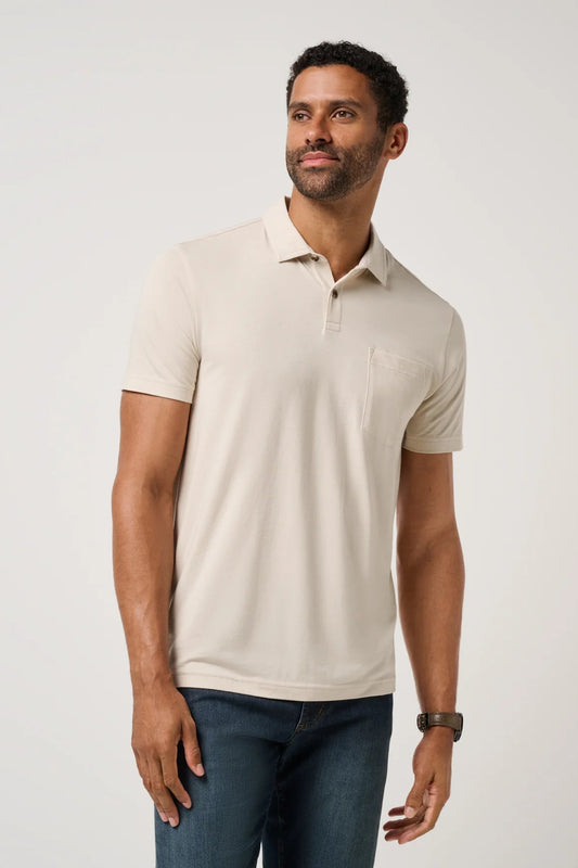 Man wearing a beige polo shirt and blue jeans on a light gray background