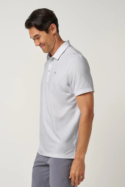A man wearing a light gray short-sleeve polo shirt and gray trousers, shown in profile against a plain light gray studio background.